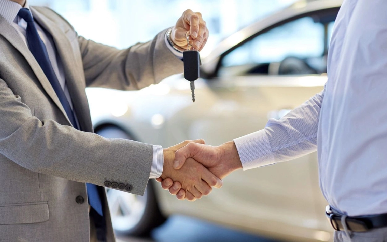 Two men shaking hands over a car with keys in hand.