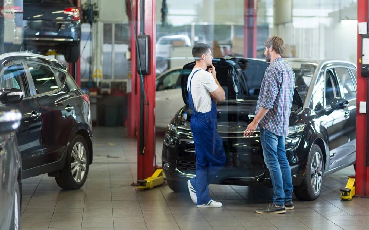 Two men in a garage talking on the phone.