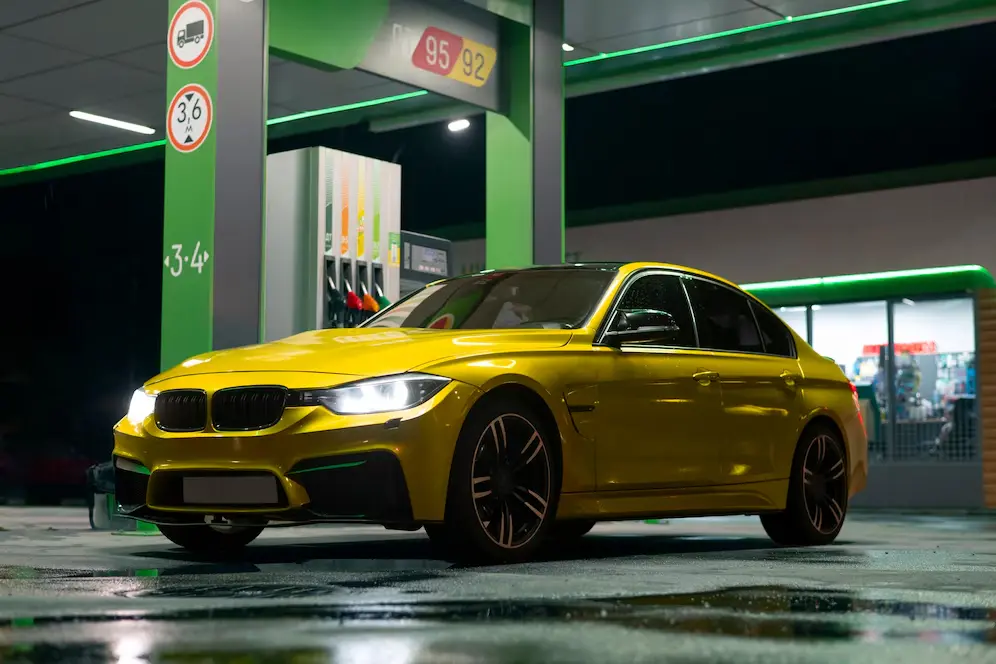 A yellow car parked in a garage next to gas pumps.