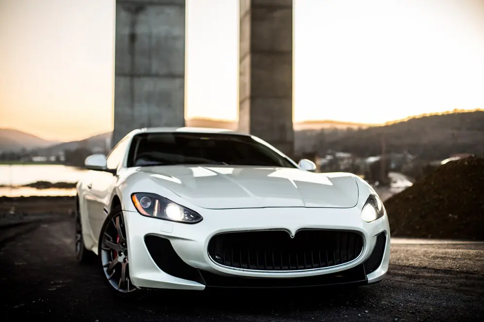 A white maserati is parked in front of some pillars.